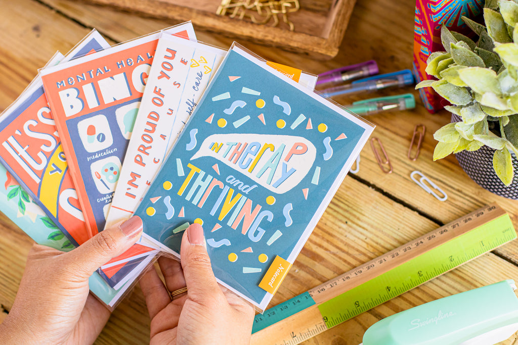 Five mental health greeting cards pictured on a wooden desk